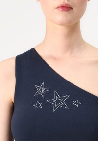 Mørkeblå topp med én skulder i myk stoff, med sølvfargede rhinestein-stjerne design i ulike størrelser på brystområdet.