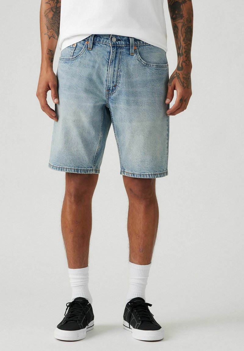 Hellblaue Jeansshorts mit geradem Schnitt, ausgefranstem Saum und Vorderentaschen, kombiniert mit schwarzen Sneakern und weißen Socken.