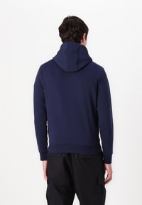 Sudadera azul marino con capucha, de textura suave, puños y dobladillo acanalados. Presenta un bolsillo tipo canguro y un ajuste relajado, vista desde atrás.