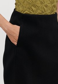 Black skirt with a smooth texture, featuring a side pocket and minimalistic design. Top in olive green with a textured pattern.