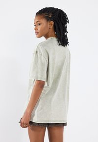 Světle zelené oversized tričko vyrobené z měkkého materiálu, které má mírně vybledlou strukturu, kleslými rameny a kulatým výstřihem.