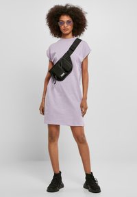 Oversized lila T-shirtjurk, korte mouwen, losse pasvorm; gecombineerd met een zwarte crossbodytas en zwarte veter enkellaarsjes.