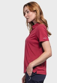 Rotes Polo-Shirt mit kurzen Ärmeln und Kragen, aus glattem Stoff gefertigt. Mit einem dezenten Markenlogo auf dem linken Ärmel und seitlichen Schlitzen für zusätzlichen Komfort.
