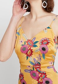 Gelbes Blumenkleid mit dünnen Trägern, das lebendige rosa und blaue Blumen zeigt, eine glatte Textur hat und eine figurschmeichelnde Silhouette bietet.
