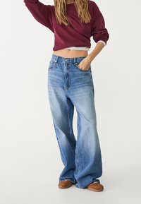 Lichtblauwe wijdere broeken van denim met een vervaagd uiterlijk. Voorzien van zijzakken en een knoopsluiting bij de taille.