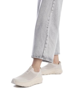 Zapatillas tipo slip-on beige con parte superior de malla, paneles texturizados y suela gruesa. Combinadas con pantalones de mezclilla ligeros en gris claro, ligeramente cortados.