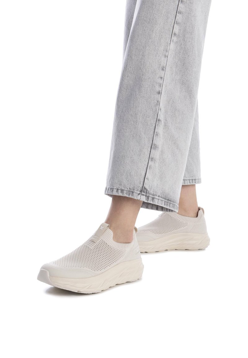 Zapatillas tipo slip-on beige con parte superior de malla, paneles texturizados y suela gruesa. Combinadas con pantalones de mezclilla ligeros en gris claro, ligeramente cortados.