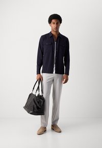 Chemise à boutons navy avec deux poches poitrine, pantalon tailoring gris clair, mocassins beiges et sac à bandoulière en cuir noir.