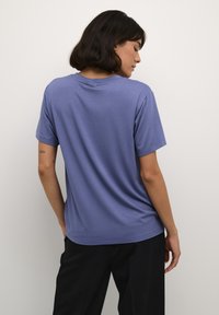 T-shirt violet à manches courtes avec un col rond, texture lisse et coupe décontractée, assortie à un pantalon noir.