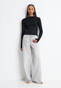 Schwarzes Langarm-Oberteil mit einem U-Boot-Ausschnitt, kombiniert mit hellgrauen, weit geschnittenen Jeans. Das Outfit hat eine glatte Textur und minimalen Detailreichtum.