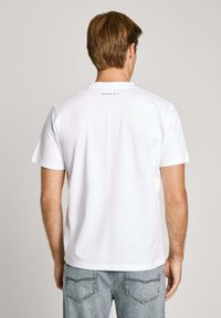 White cotton t-shirt with short sleeves. Features a small black text print at the upper back. Soft texture, classic crew neckline.