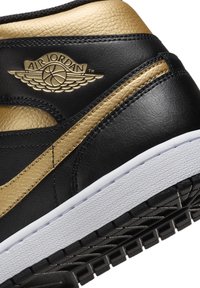 Crne i zlatne kožne tenisice s teksturiranim završetkom, s bijelim srednjim potplatom i crnim gumenim potplatom. Upečatljen Air Jordan logo.