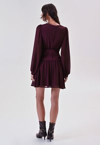 Bordeaux jurk met lange pofmouwen, een cinched taille en een geplooide rok. Gecombineerd met zwarte enkelboots met metalen accenten.