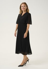 Melnas kroku midi kleitas ar īsām caurspīdīgām piedurknēm un apvelkamā stila bodi. Apvienota ar melniem slingback augstpapēžu apaviem ar zelta akcentu.