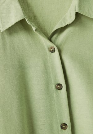 Camisa de botonadura verde hecha de una tela ligera con un acabado texturizado. Presenta un cuello y tres botones marrones a lo largo de la tapeta.