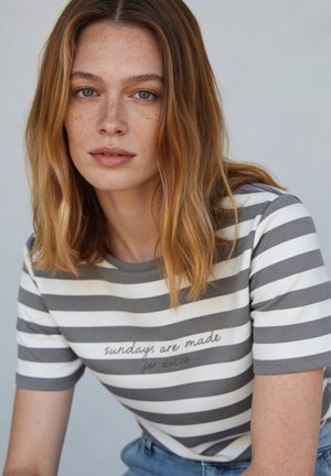 Jeune femme aux cheveux châtain clair et aux taches de rousseur porte un t-shirt rayé gris et blanc avec le texte « sundays are made for dolce ».