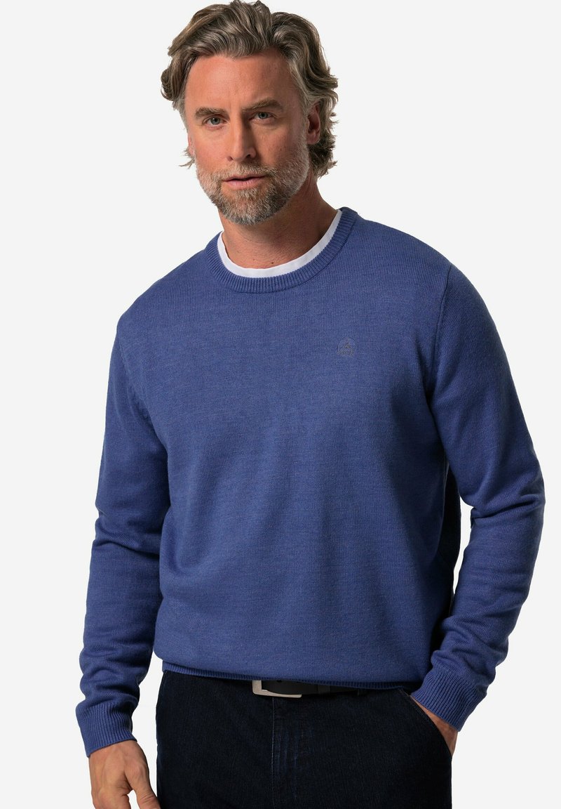 Blå stickad tröja med långa ärmar, ribbad mudd och halsringning, med en diskret logotyp på bröstet. Kombineras med mörka jeans.