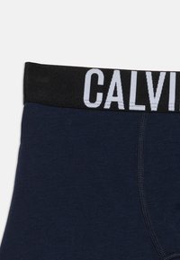 Μπόξερ σε ναυτικό μπλε χρώμα με μαύρη μέση που διαθέτει μεγάλο λευκό μερικό λογότυπο "CALVIN" και εμφανείς ραφές στην μπροστινή πλευρά.