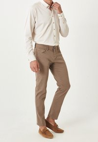 Pantalones de algodón color beige con un corte recto, combinados con una camisa de botones color beige claro y zapatos de mocasín marrones. Presentan detalles de botones y un diseño elegante.