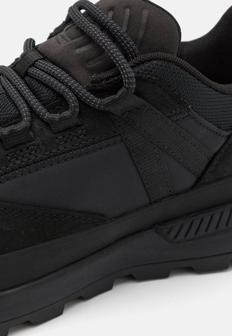 Sneaker nera texturizzata che presenta una combinazione di materiali in suede e mesh, lacci tondi e una suola robusta con motivi di grip.