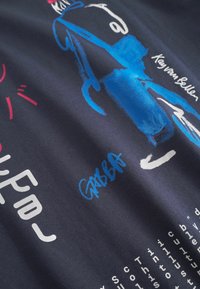 Námornícky tričko s pestrou grafikou postavy na kolobežke, s bielym a červeným textom. Podpis "GABBA" vo svetlo modrej na spodnej strane.