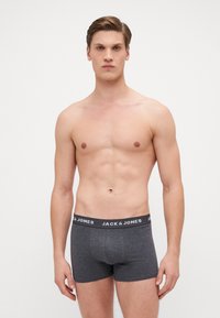Graue Boxershorts mit einem schwarzen elastischen Bund, auf dem "JACK & JONES" steht. Der Stoff hat eine glatte Textur und ein tailliertes Design.