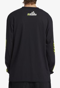 Μαύρο πουκάμισο με μακρύ μανίκι και στρογγυλή λαιμόκοψη, διαθέτει το λογότυπο DC Racing στην πλάτη και έντονες φωσφοριζέ πράσινες λεπτομέρειες στα μανίκια.