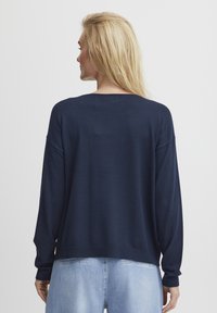 Granatowy sweter dżersejowy o luźnym kroju, z opadającymi ramionami i prążkowanymi mankietami. Materiał wydaje się miękki o gładkiej fakturze. Widok z tyłu.