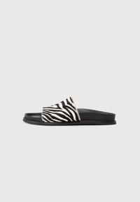 Svart och vit zebratryck slide-sandaler med en mjuk texturerad ovandel och en slät svart gummisula, designade för enkel att ta på.