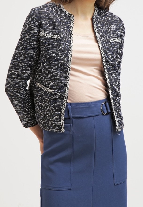 Marinblå texturerad jacka med ett vävt mönster, med metalltråd accenter, rund krage och två framfickor. Bärs över en beige topp.