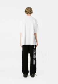 Camiseta blanca oversize con escote redondeado, combinada con pantalones negros que cuentan con etiquetas impresas y acentos. Textura de algodón suave, corte relajado.