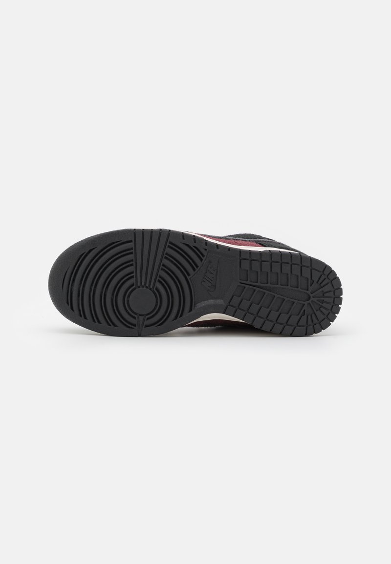 Schwarze Sneaker-Sohle mit einem strukturierten Muster, das ein zirkuläres Logo zeigt. Das Design umfasst Rottöne und Grautöne im oberen Bereich.