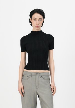 Black ribbed knit top with short sleeves and a high neckline, featuring a slightly cropped hem. Paired with light gray high-waisted pants.