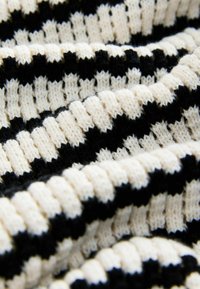 Gros plan sur un tissu maille doux avec des rayures côtelées noires et blanches alternées formant un motif horizontal.