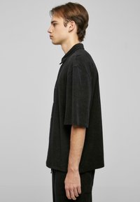Camisa negra de manga corta y botones, hecha de una tela suave, con un corte relajado y un cuello. Diseño simple sin patrones ni acentos.