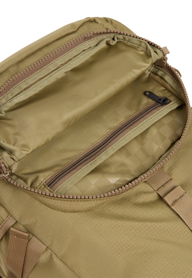 Interior de una mochila de tela caqui con un compartimento principal y un pequeño bolsillo con cremallera, que presenta un forro texturizado y detalles en cremallera beige.