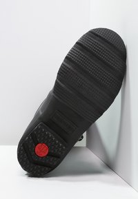 Suela de bota de goma negra con patrones de agarre texturizados, que presenta un acento circular rojo y el nombre de la marca en relieve "HUNTER".