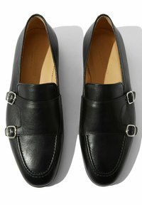 Crne kožne loafers cipele s dvostrukim kopčama, okruglim vrhom i glatkom teksturom. Unutrašnjost s mekim oblogom za udobnost.