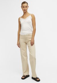 Hvid cami med blonder, beige lige ben bukser og sorte sandaler. Glat stof, afslappet pasform, subtile sømme og frontlommer.