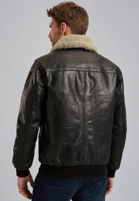 Chaqueta de cuero negra con cuello de borrego, puños y cintura acanalados. Textura suave con costuras visibles y un diseño casual.
