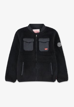 Svart fleece-jakke med glidelås foran, rund krage, to brystlommer, sidelommer og et logo-merke på venstre arm. Myk tekstur.
