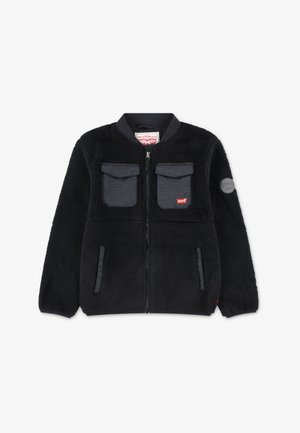 Casaco de fleece preto com fecho na frente, gola redonda, dois bolsos no peito, bolsos laterais e um patch de logo no braço esquerdo. Textura suave.