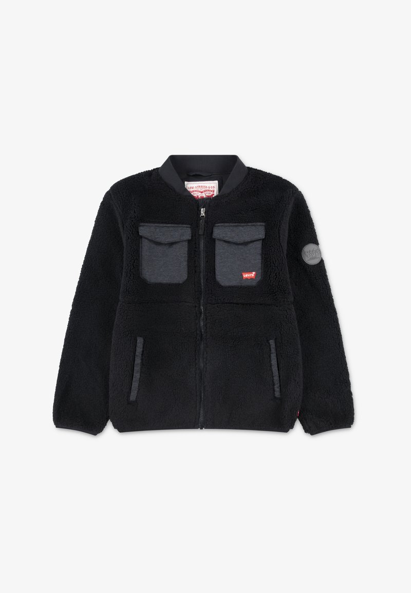 Must värvi fliisjakker, millel on lukuga esiosa, ümar kaelus, kaks rinnataskut, küljetaskud ja logo patch vasakul käisel. Pehme tekstuur.