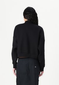 Felpa nera corta con maniche lunghe, polsini e orlo a costine, realizzata in tessuto morbido. Indossata con pantaloni cargo neri dotati di tasche.