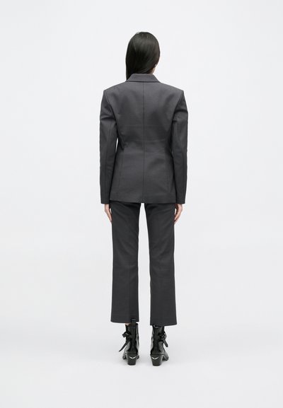 Ραμμένο γκρι σακάκι και �αντίστοιχες παντελόνες, δομημένη σιλουέτα, απαλός υφασμάτινος χαρακτήρας, ολοκληρωμένο με γυαλιστερά μαύρα μποτίνια με φιόγκους.