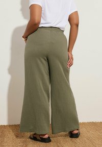 Korkea vyötärö, leveälahkeiset housut, jotka on valmistettu teksturoidusta oliivinvihreästä kankaasta. Varustettu joustavalla vyötärönauhalla ja yhdistetty mustiin sandaaleihin.