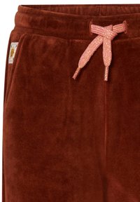 Bruna velourbyxor med en texturerad yta, med en matchande rosa dragsko och en etikett på midjebandet.