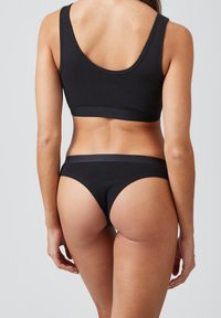 Zwart katoenen sportbeha en bikini slip set met een naadloos ontwerp en elastische banden, die een gladde textuur en eenvoudige silhouet tonen.