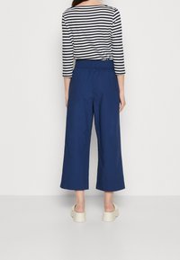 Marineblauwe wijde broek met een elastische tailleband, gecombineerd met een zwart-wit gestreepte top met driekwartmouwen, met een gladde textuur.