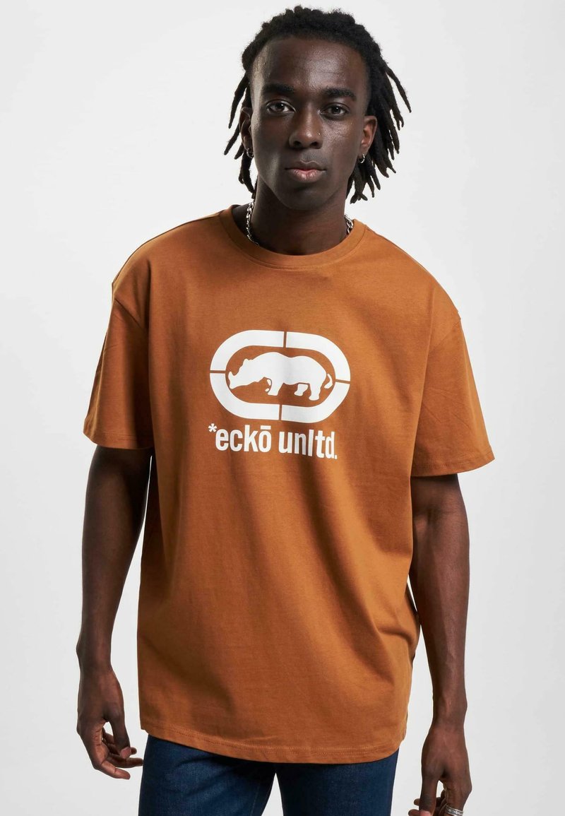 Brun bomulds T-shirt med en hvid grafik af en næsehorn og teksten "*eckō unlt.d." på forsiden. Korte ærmer, rund halsudskæring.